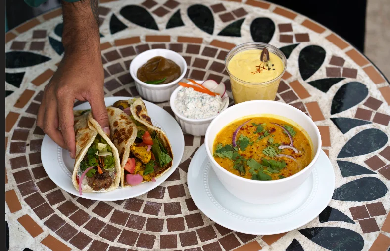 Sheesh food spread featuring kebab rolls, daal, and mango lassi